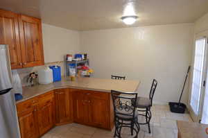 Kitchen featuring freestanding refrigerator, a peninsula, light countertops, brown cabinets, and a textured ceiling