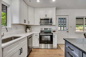 Kitchen with stainless steel appliances, a sink, recessed lighting, white cabinetry, and light wood-type flooring