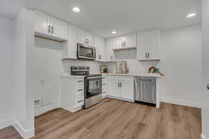 Kitchen featuring stainless steel appliances, a sink, baseboards, recessed lighting, and white cabinetry
