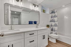 Bathroom featuring double vanity, toilet, shower / tub combo with curtain, and wood finished floors
