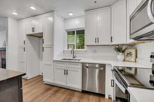 Kitchen featuring appliances with stainless steel finishes, a sink, a textured ceiling, light wood-type flooring, and white cabinets