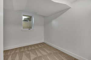 Empty room featuring carpet floors, baseboards, and vaulted ceiling