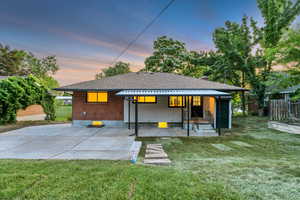 Back of house at dusk with a shingled roof and a patio
