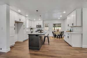Kitchen with appliances with stainless steel finishes, recessed lighting, baseboards, white cabinetry, and wood finished floors