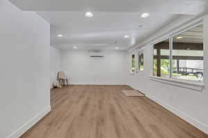 Empty room with a wall mounted AC, recessed lighting, light wood-type flooring, and baseboards