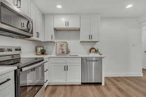 Kitchen featuring stainless steel appliances, a sink, light countertops, light wood-type flooring, and baseboards