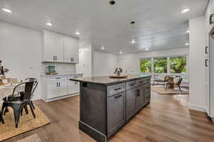 Kitchen featuring light wood-type flooring, white cabinets, a center island, baseboards, and recessed lighting