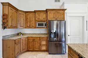 Kitchen featuring appliances with stainless steel finishes, brown cabinets, and light tile patterned flooring