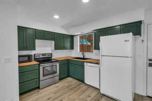 Kitchen featuring white appliances, green cabinets, butcher block counters, a sink, and light wood-style flooring