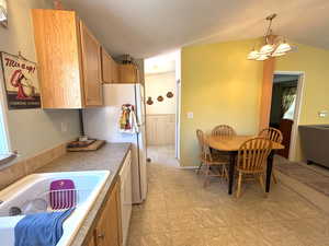Kitchen with a chandelier, decorative light fixtures, freestanding refrigerator, vaulted ceiling, and a sink