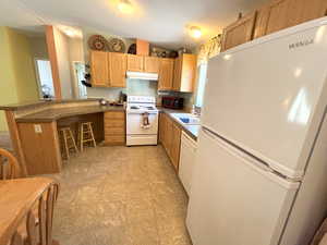 Kitchen featuring white appliances, under cabinet range hood, a sink, a peninsula, and a breakfast bar area