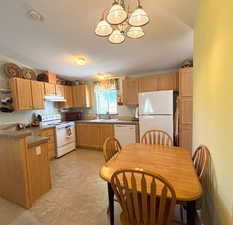 Kitchen featuring white appliances, a chandelier, under cabinet range hood, a sink, and dark countertops