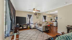 Living area featuring light wood flooring, a ceiling fan, a chandelier, crown molding, and baseboards