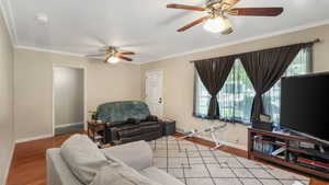 Living room featuring a ceiling fan, crown molding, baseboards, and wood floors