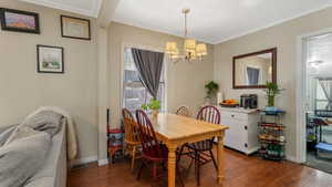 Dining room featuring a chandelier, wood floors, ornamental molding, healthy amount of natural light, and baseboards