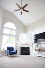Carpeted living area with a tile fireplace, high vaulted ceiling, ceiling fan, and baseboards