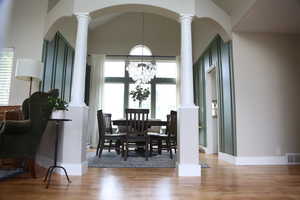 Dining area featuring ornate columns, light wood-style flooring, arched walkways, vaulted ceiling, and a chandelier