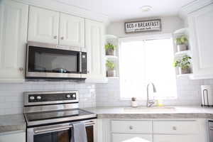 Kitchen with open shelves, appliances with stainless steel finishes, a sink, and white cabinetry