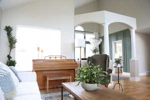 Living area with decorative columns, vaulted ceiling, arched walkways, wood finished floors, and baseboards