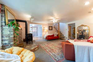 Carpeted living room with a wood stove, ceiling fan, and baseboards