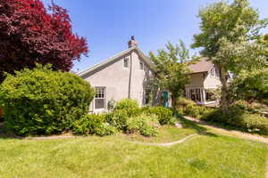 Back of house featuring a chimney, stucco siding, and a lawn
