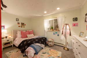 Carpeted bedroom with a baseboard radiator, recessed lighting, ornamental molding, and baseboards
