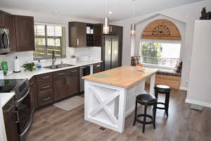 Kitchen featuring appliances with stainless steel finishes, a sink, dark brown cabinets, a kitchen bar, and wood finished floors