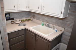 Kitchen with light countertops, a sink, white cabinets, tasteful backsplash, and gray cabinets