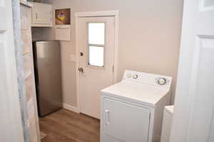 Washroom with cabinet space, separate washer and dryer, wood finished floors, and baseboards