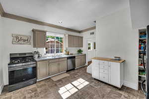 Kitchen featuring appliances with stainless steel finishes, baseboards, a sink, ornamental molding, and light countertops