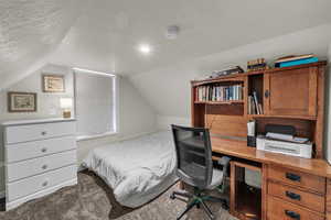 Bedroom featuring a textured ceiling, lofted ceiling, carpet floors, and a desk