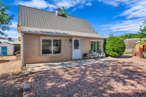 Back of property featuring stucco siding, a patio area, metal roof, and a chimney