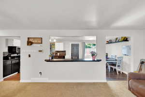 Kitchen featuring stainless steel microwave, electric range oven, carpet flooring, white cabinets, and baseboards