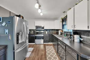 Kitchen with appliances with stainless steel finishes, a sink, dark countertops, wood finished floors, and white cabinetry