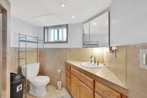 Bathroom featuring tile walls, vanity, tile patterned flooring, toilet, and a wainscoted wall