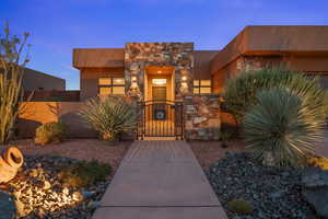 Doorway to property featuring a gate, stone siding, and stucco siding