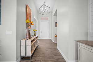 Hall featuring a chandelier, dark wood-type flooring, and baseboards
