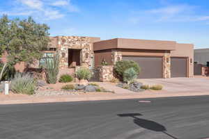 Pueblo-style house with stucco siding, an attached garage, stone siding, and driveway