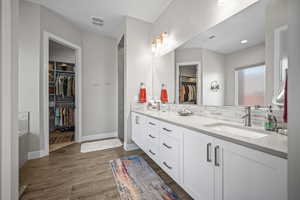 Bathroom featuring double vanity, wood finished floors, a spacious closet, decorative backsplash, and baseboards