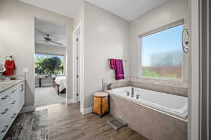 Full bath featuring connected bathroom, a garden tub, vanity, ceiling fan, and wood finished floors