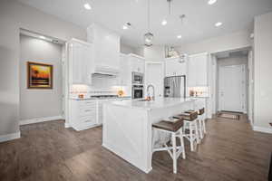 Kitchen featuring appliances with stainless steel finishes, a sink, baseboards, backsplash, and dark wood finished floors