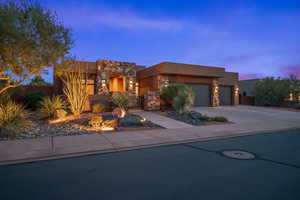 Pueblo revival-style home with stucco siding, concrete driveway, an attached garage, and stone siding