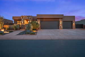 Pueblo revival-style home featuring a gate, an attached garage, stone siding, stucco siding, and driveway
