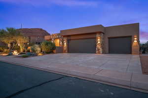 Pueblo-style house featuring a garage, stone siding, concrete driveway, and stucco siding