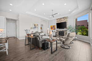 Living room featuring a raised ceiling, ceiling fan, recessed lighting, a stone fireplace, and baseboards