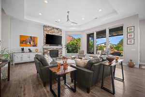 Living area with a tray ceiling, ceiling fan, dark wood-style flooring, recessed lighting, and a fireplace