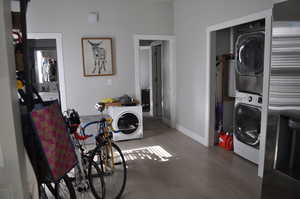 Washroom featuring stacked washer and clothes dryer, wood finished floors, and baseboards
