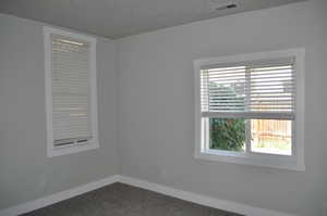 Spare room featuring dark colored carpet, baseboards, and a textured ceiling