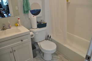 Full bath with marble look tiles, vanity, toilet, and shower / tub combo with curtain