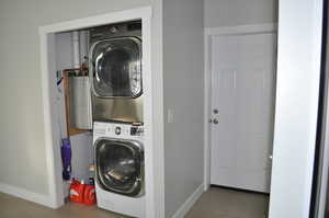 Washroom featuring stacked washer / drying machine, wood finished floors, and baseboards